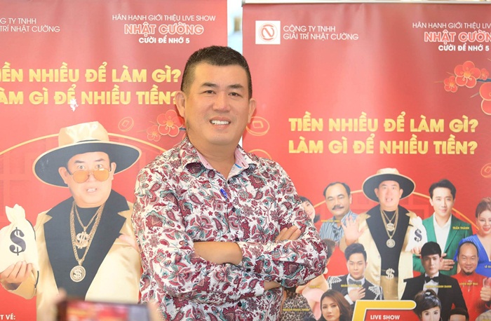 Danh hài Nhật Cường với Poster phía sau có các gương mặt trong phim Nhà Bà Nữ: Việt Anh, Trấn Thành, Lê Giang